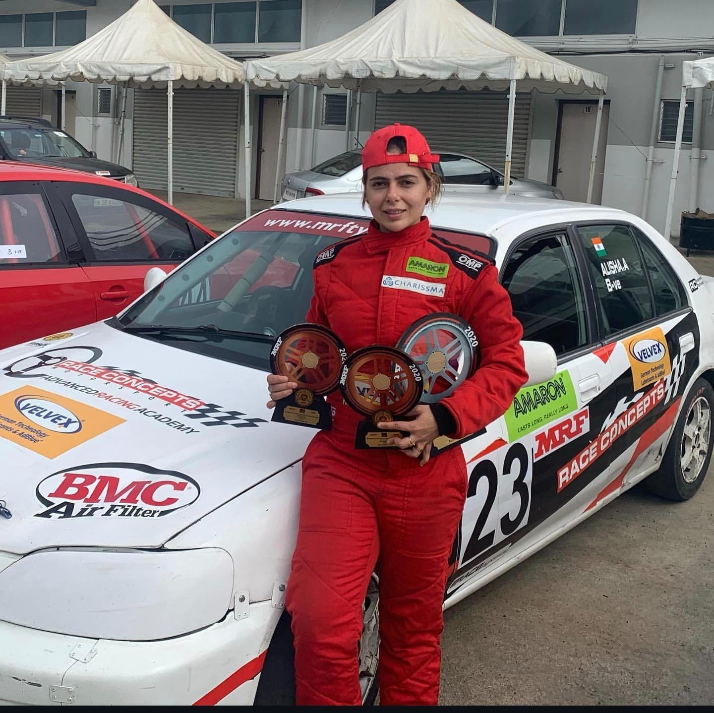 Alisha Abdullah in red racing suit with trophies