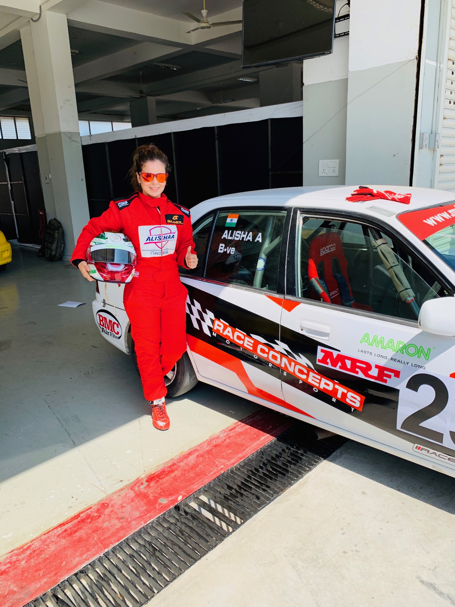 Alisha thumbs up next to race car